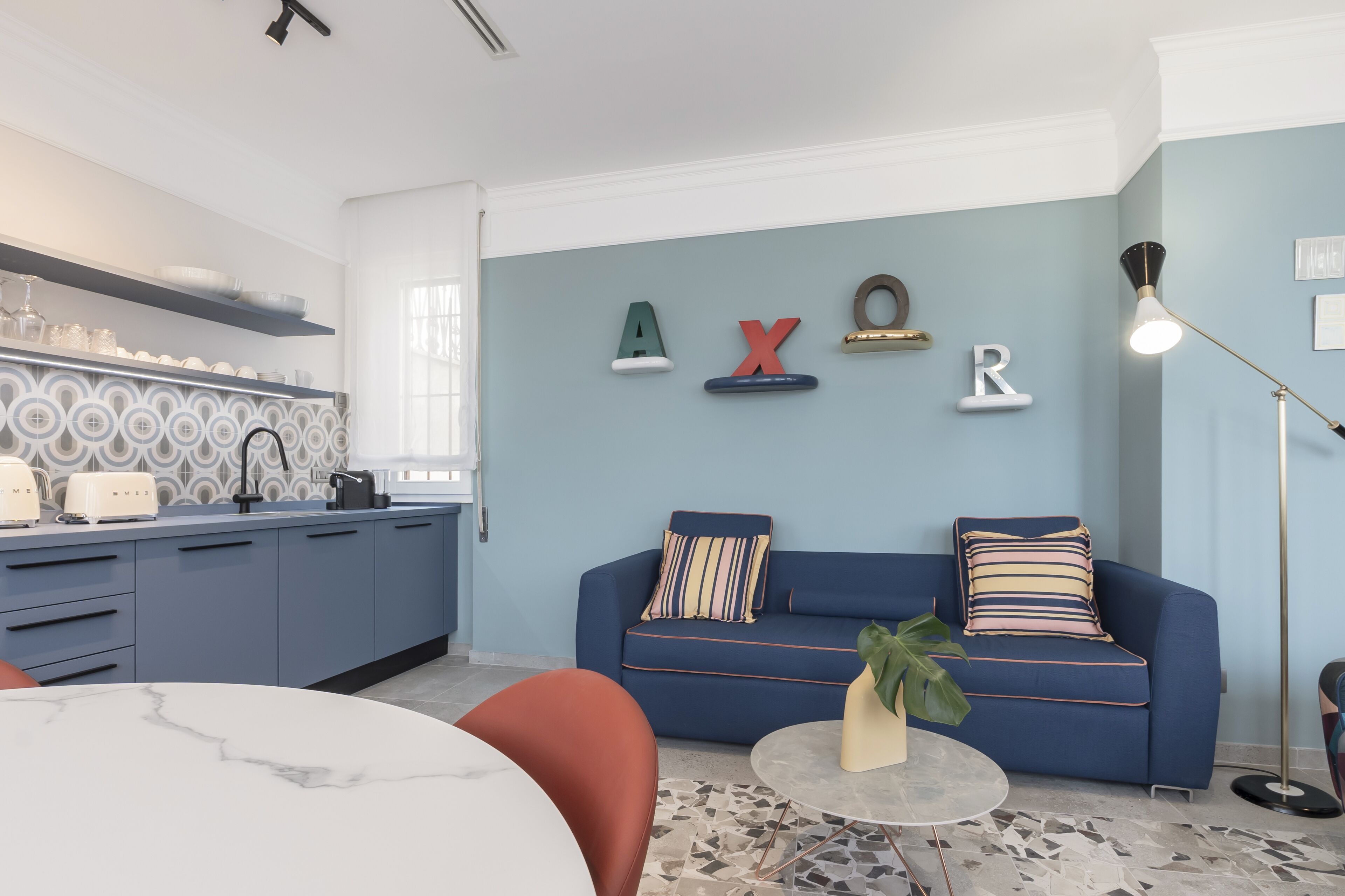 A modern living room with a blue sofa, a coffee table, and a kitchen area with blue cabinets and decorative items.