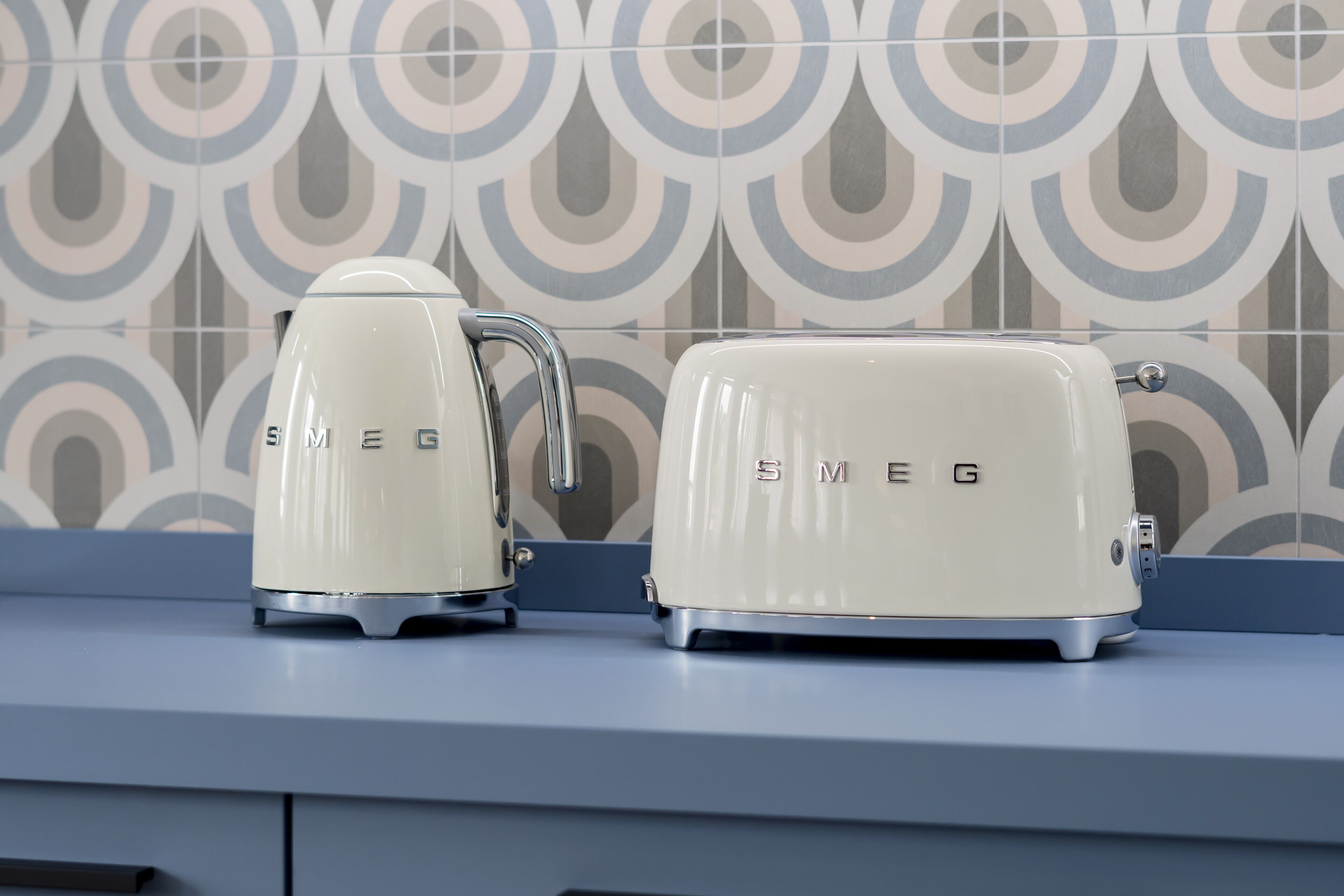 Two vintage-style toasters on a kitchen counter with a patterned backsplash.