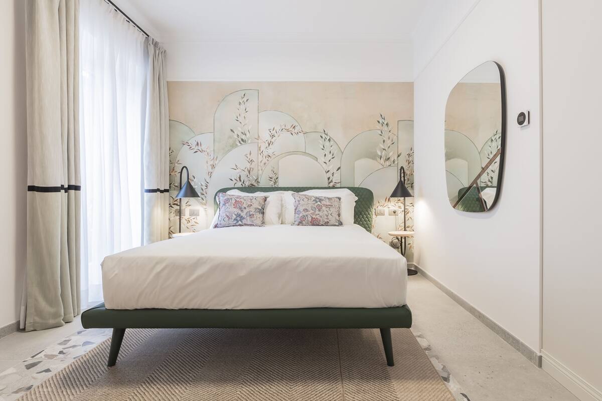 Une chambre à coucher bien aménagée, avec un lit, des lampes de chevet, un miroir et une tête de lit décorative.
