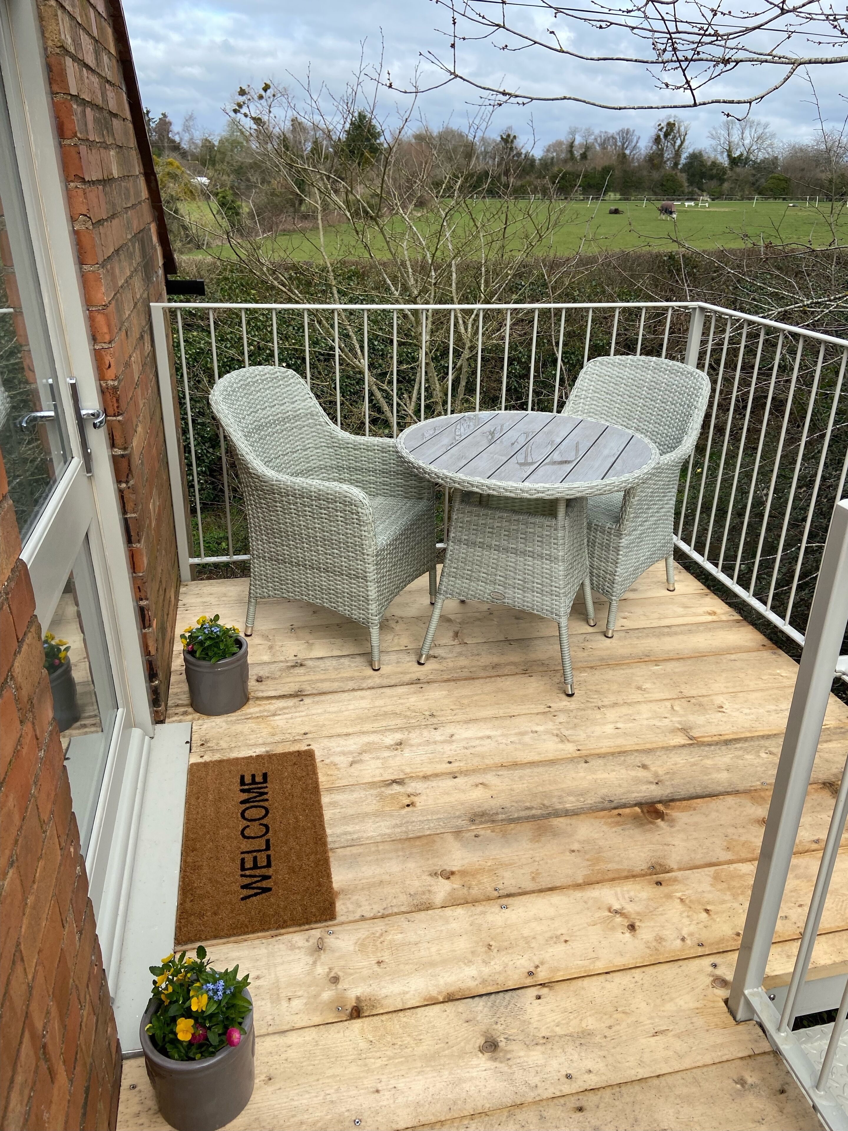 A balcony with wicker furniture, a welcome mat, and potted plants.