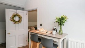 A kitchen with a white door, a wooden countertop, a coffee maker, a vase with flowers, and a loaf of bread.