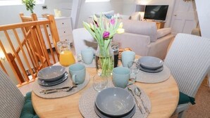 A dining table set with plates, cups, and cutlery, surrounded by chairs with green cushions.