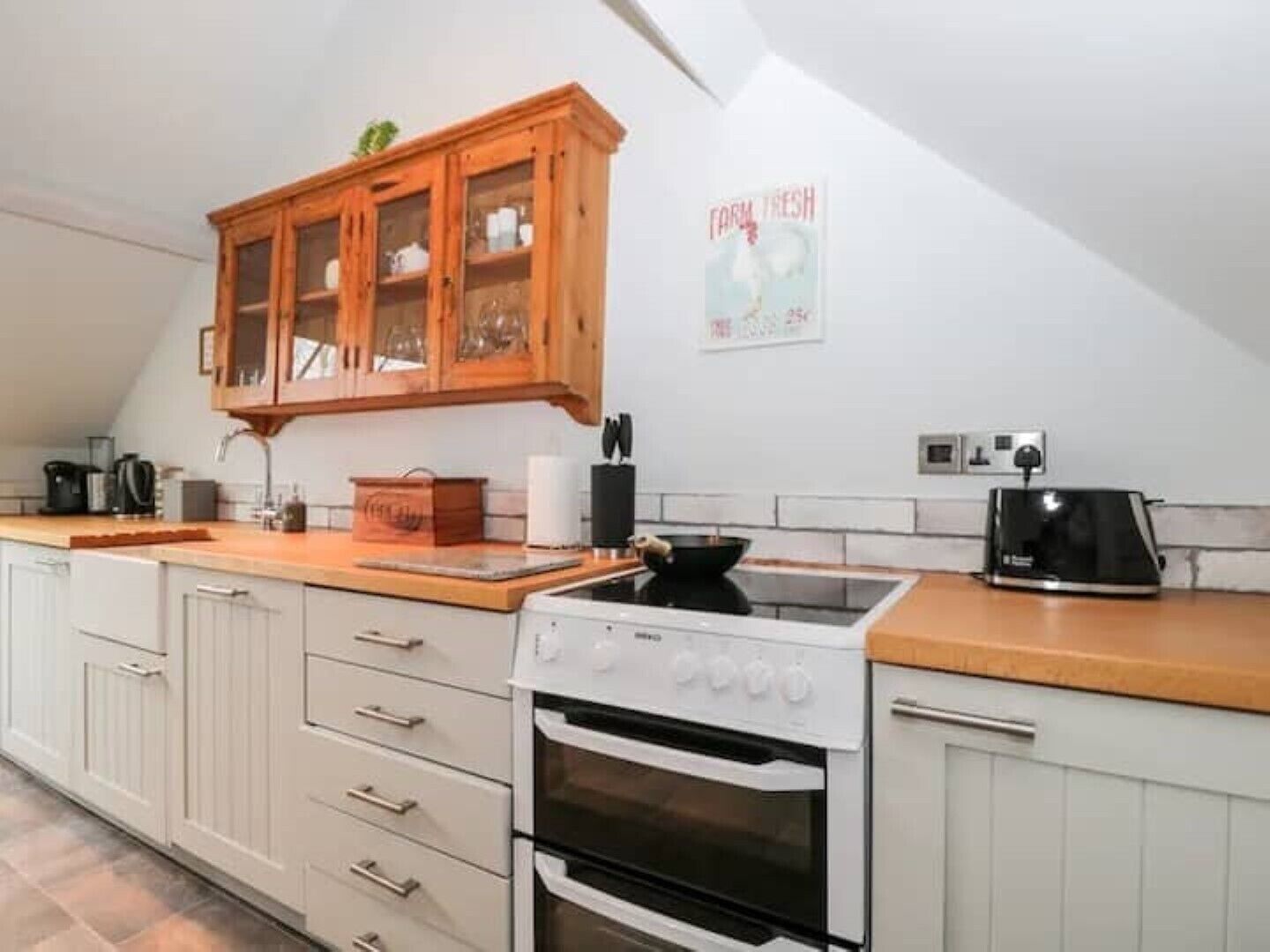 Une cuisine avec des meubles blancs, un meuble en bois doté de portes en verre, une cuisinière et une bouilloire.