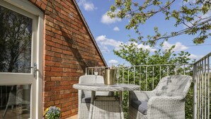 A balcony with wicker furniture, a glass table, and a metal chair.