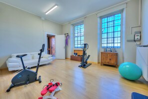 A spacious living area with a white sofa, an exercise bike, a stationary bike, a large exercise ball, and a wooden cabinet.