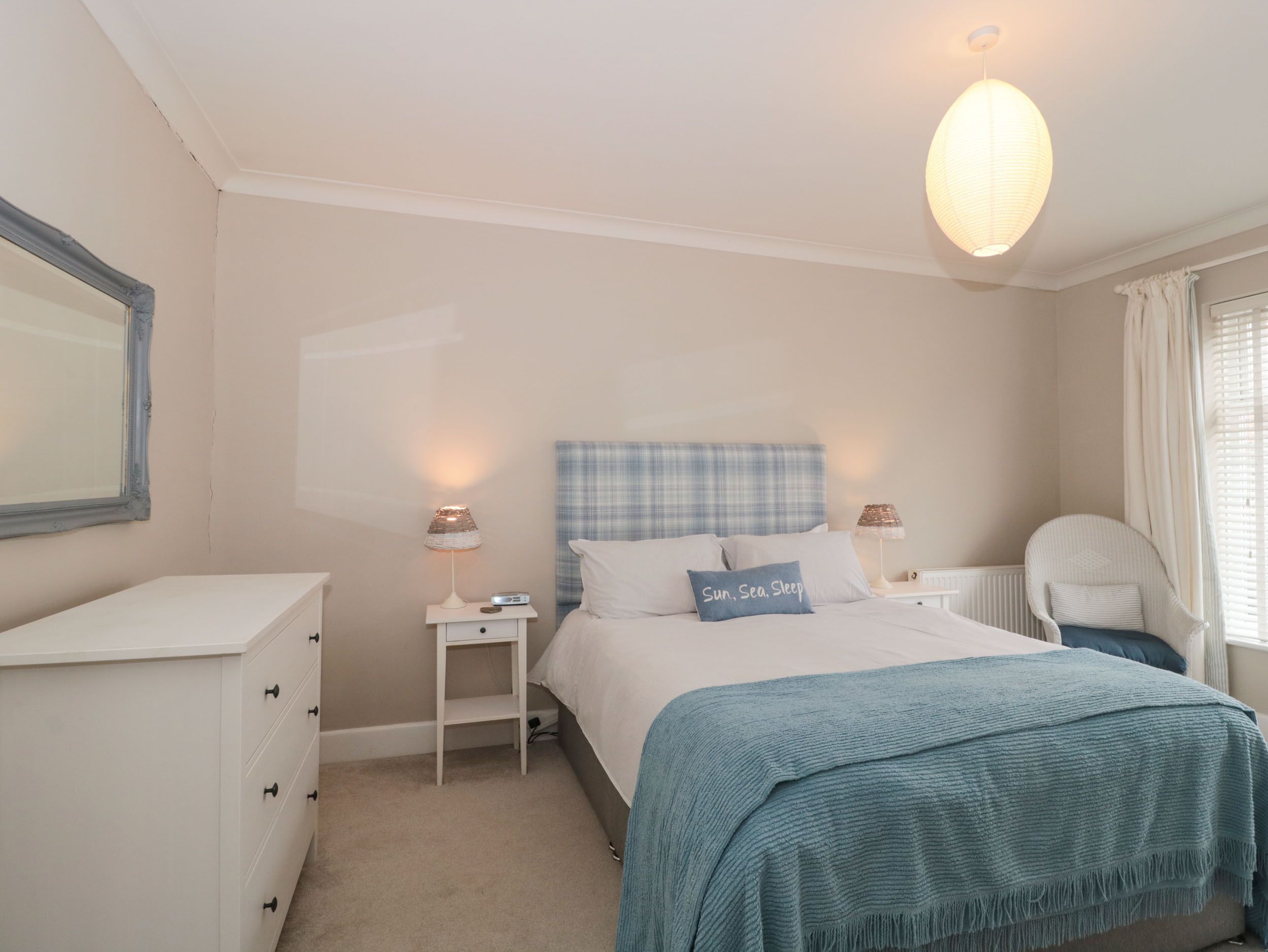 Een slaapkamer met een bed, nachtkastjes, een stoel, een dressoir en een hanglamp.