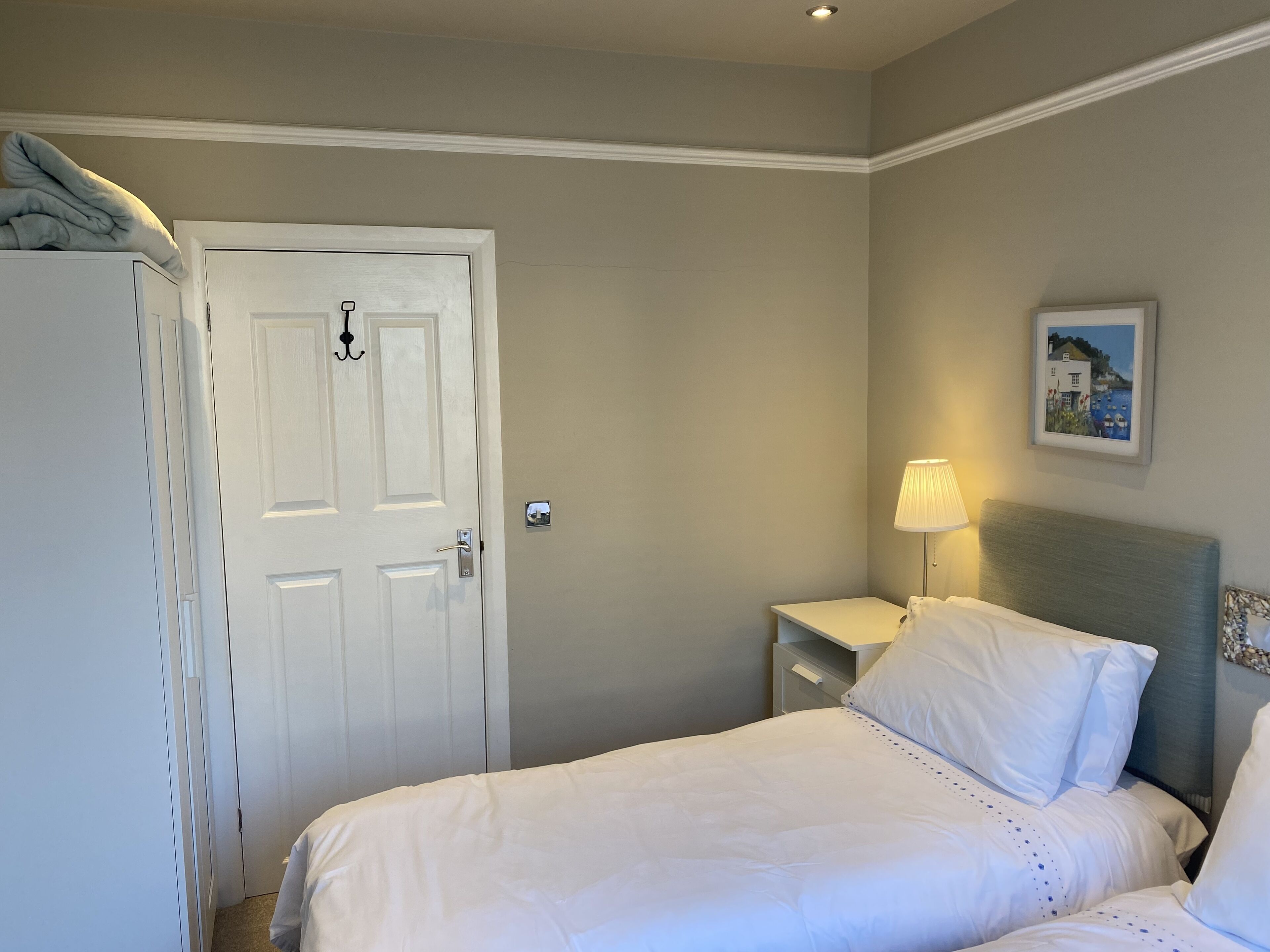 A bedroom with a bed, a nightstand, a lamp, a door, and a picture on the wall.