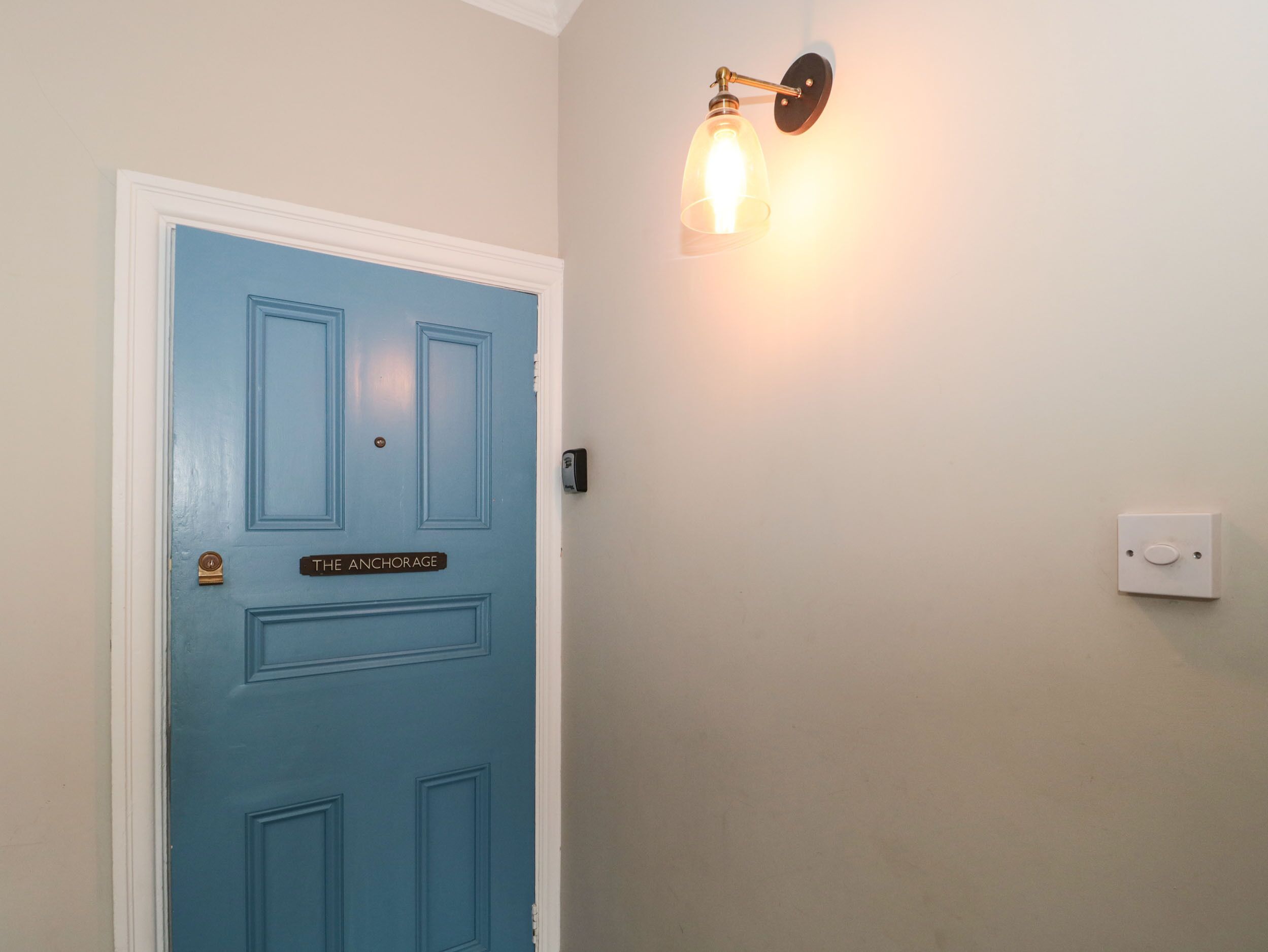 Een blauwe deur met een bord waarop 'THE ANCHORAGE' staat en een wandlamp.