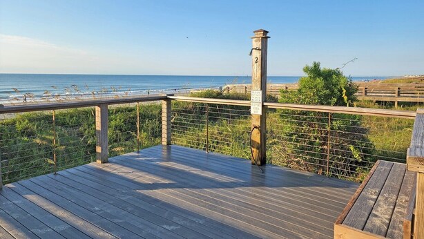 Une terrasse en bois avec une balustrade donnant sur une plage.