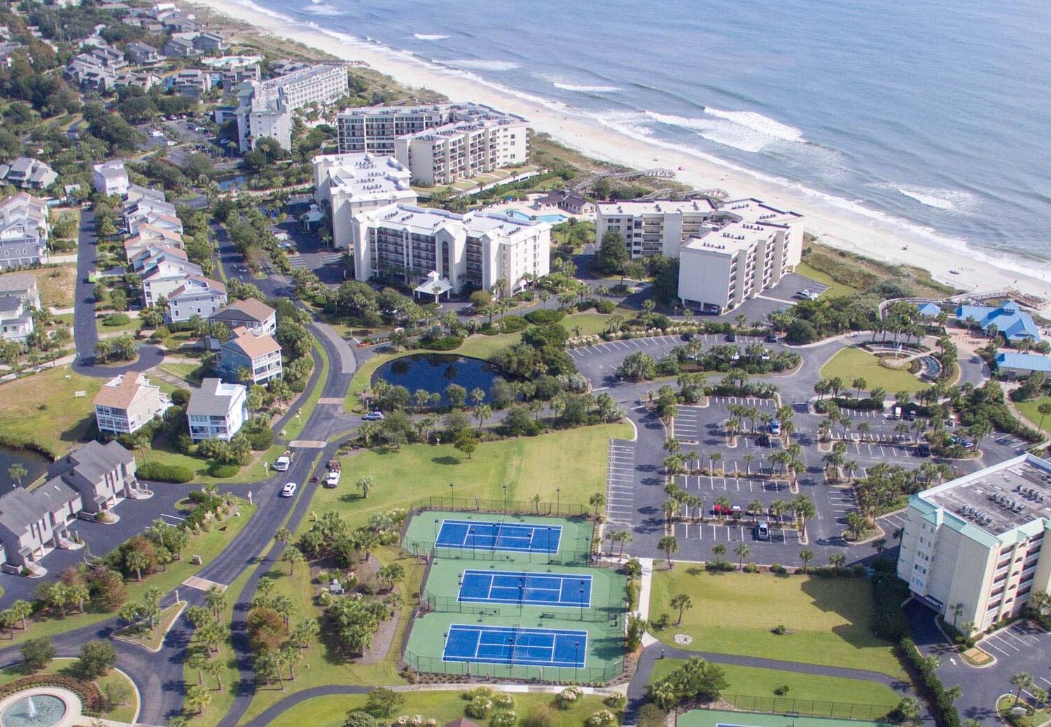 Vue aérienne d’un quartier résidentiel situé sur la côte, avec de nombreux immeubles d’appartements, une plage et des courts de tennis.