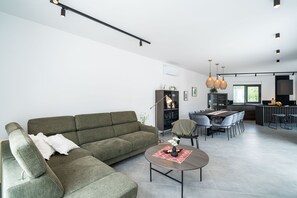 A modern living room with a sectional sofa, a coffee table, and a dining area with chairs and a table. - Villa Luce (Cilipi)