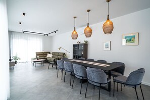 A modern dining area with a long table, grey upholstered chairs, and three hanging pendant lights. - Villa Luce (Cilipi)