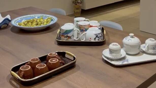 Un coin repas agrémenté d’un mur en pierre, d’un téléviseur diffusant une image de cheminée et d’une table mise avec de la vaisselle et des théières.