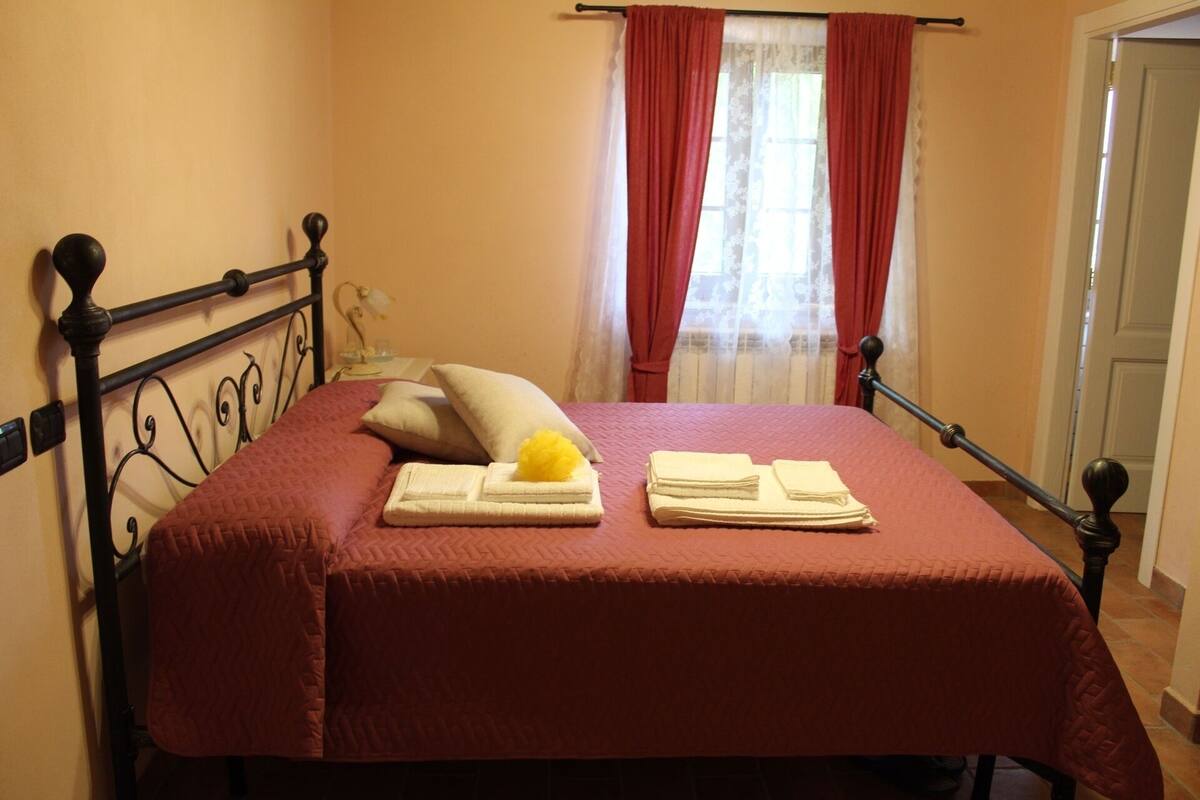 Een net opgemaakt bed met een rode dekbedovertrek, kussens en opgevouwen handdoeken.