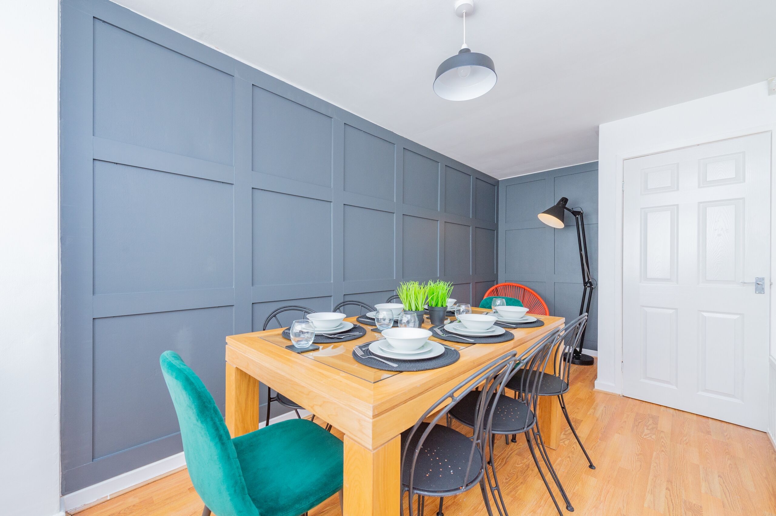 A dining area with a wooden table set for four, surrounded by teal chairs.