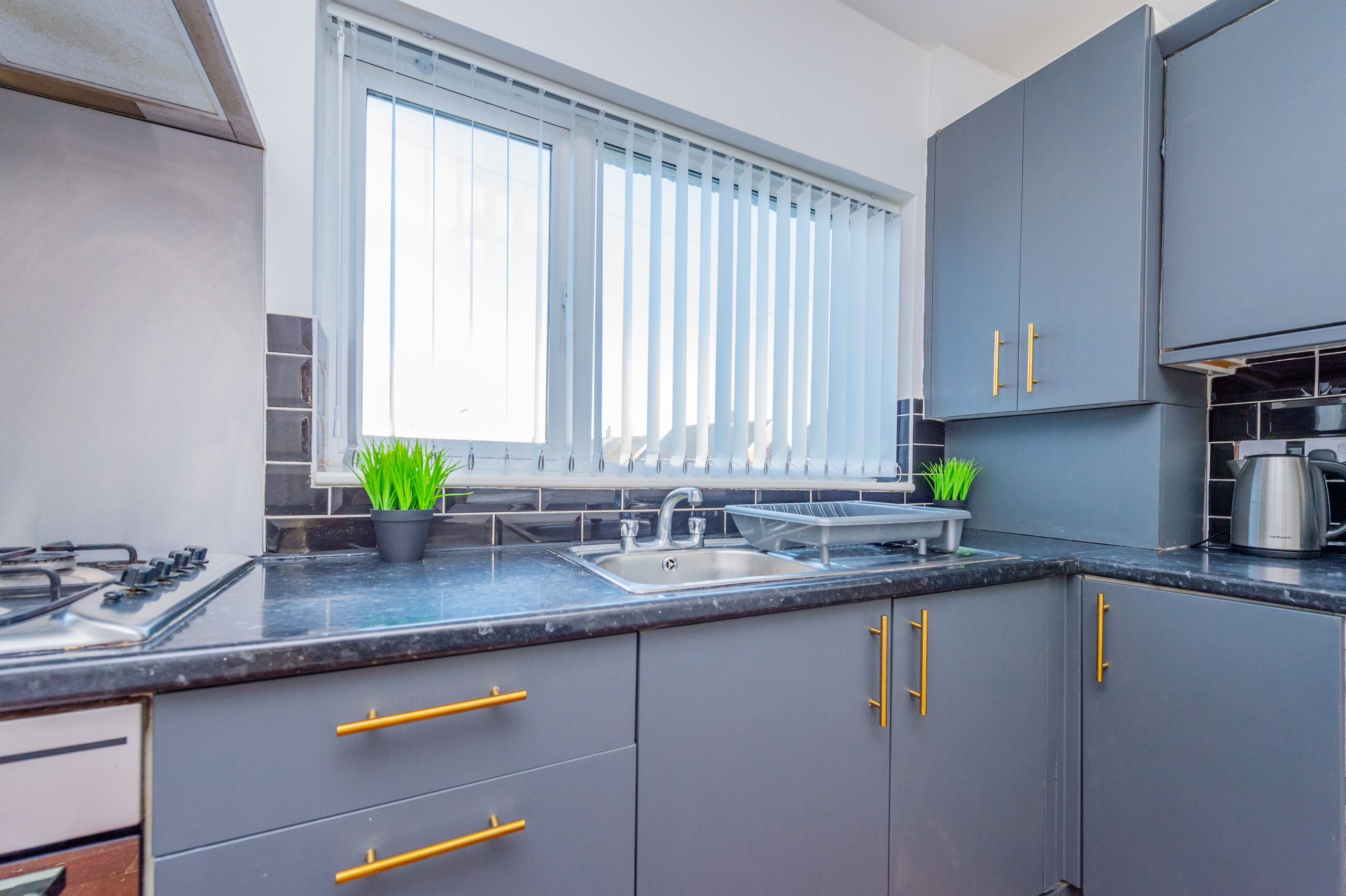 A modern kitchen with grey cabinets, a stainless steel sink, and a window with blinds.