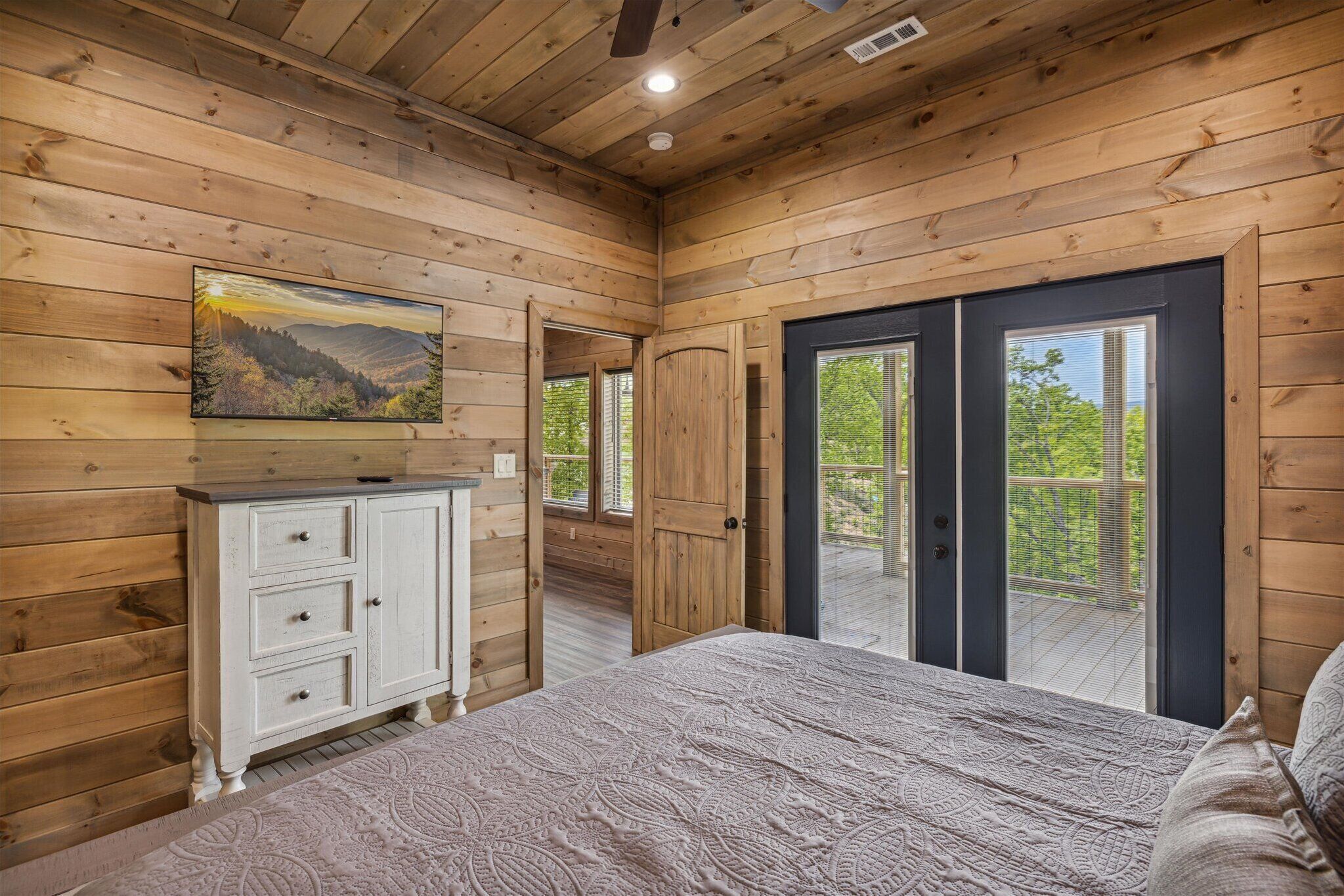 Une chambre aménagée dans une cabane en bois, avec un lit, une commode et une porte-fenêtre coulissante donnant sur un balcon.