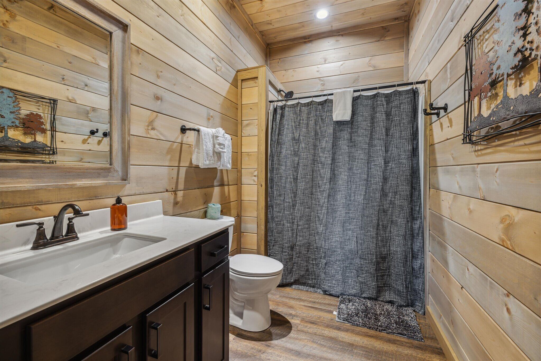 A wooden cabin bathroom with a sink, toilet, and shower curtain.