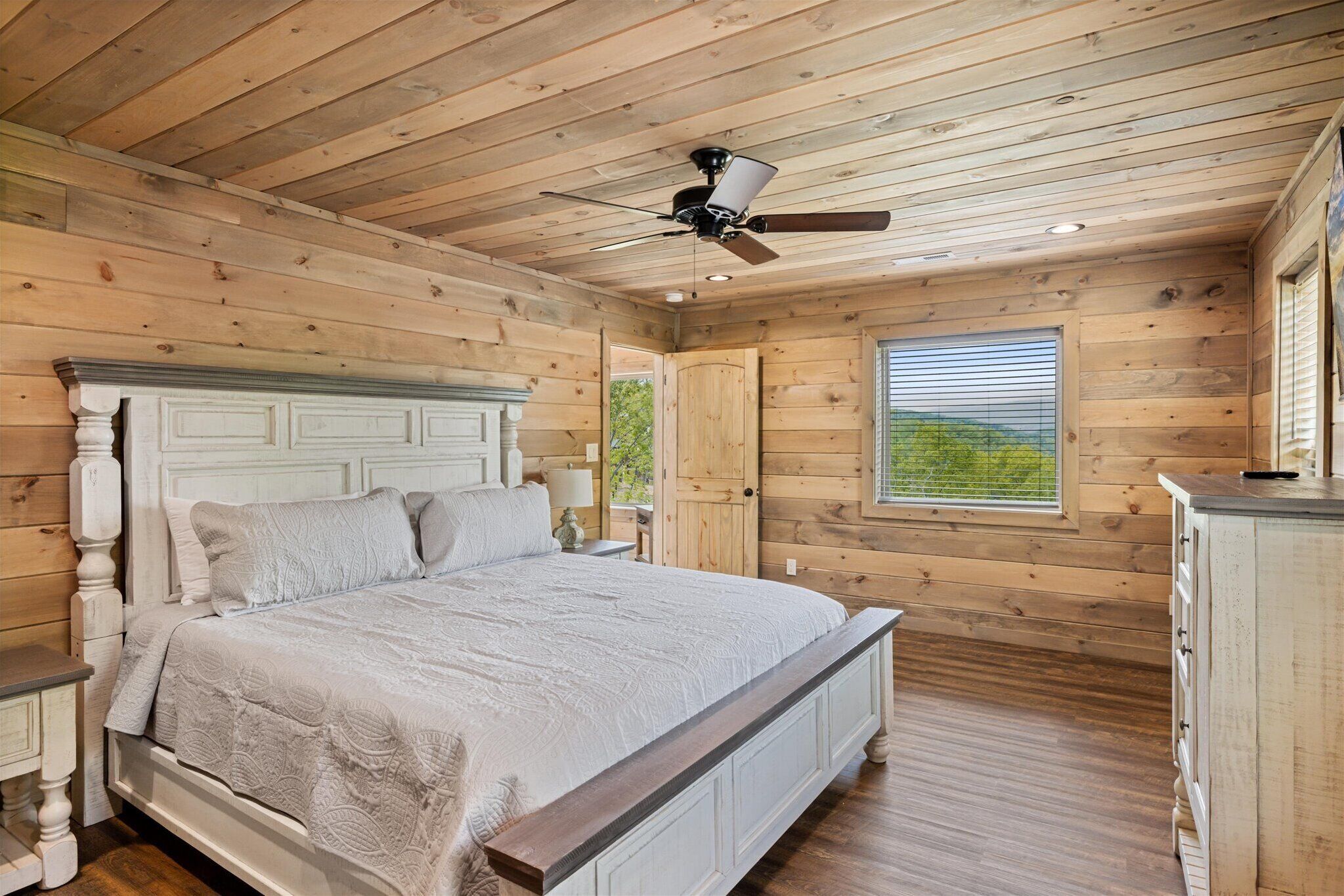 A wooden cabin bedroom with a bed, a ceiling fan, and a window.