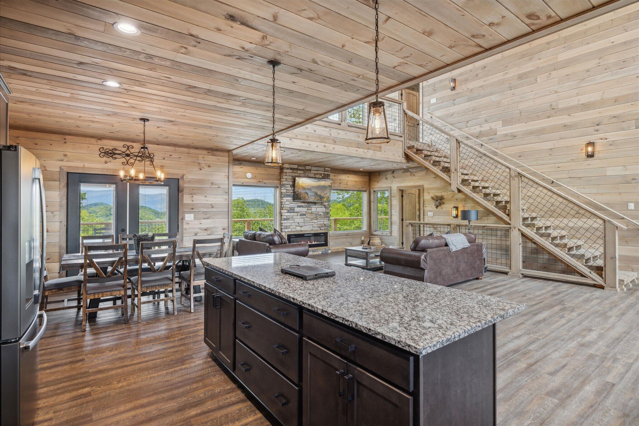 A spacious kitchen with a large island, wooden ceiling, and a staircase leading to an upper level.