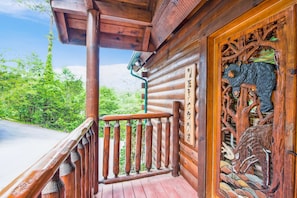 Une cabane en bois dotée d’un balcon, d’une porte en bois sculpté et offrant une vue sur la verdure.