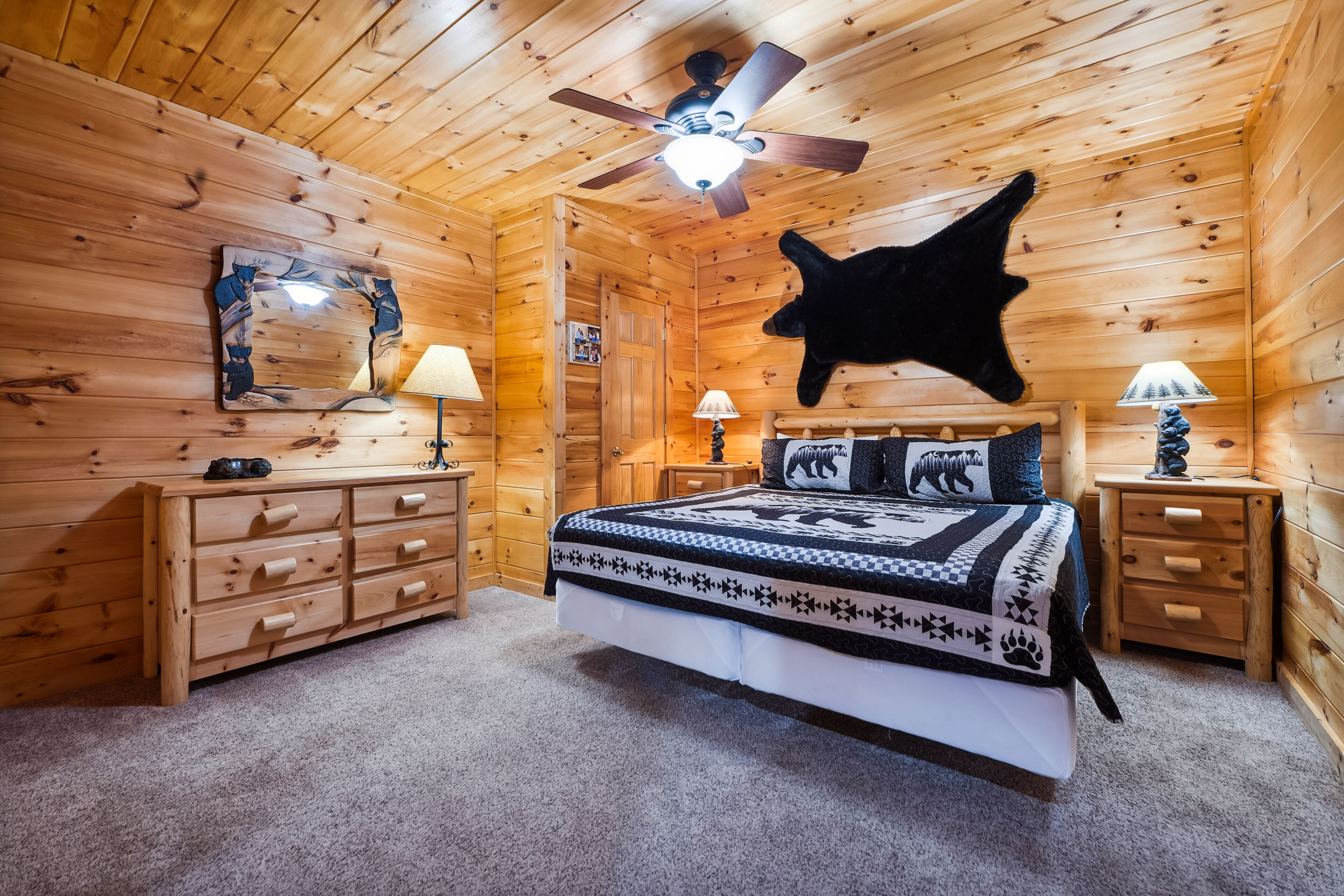 A log cabin bedroom with a bed, wooden dresser, and a ceiling fan.