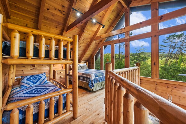 Une cabane en bois avec une chambre à l’étage et un balcon donnant sur une forêt.