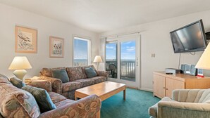 Un salon comprenant un ensemble de canapés, une table basse, un téléviseur et une vue sur la plage, visible à travers la porte-fenêtre coulissante.