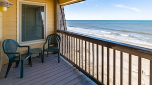 Una terraza de madera con dos sillas y una mesa, con vistas a una playa y olas.