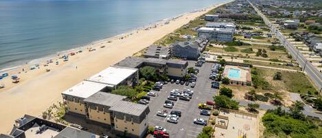 An aerial view of a coastal area with a beach, parking lot, and buildings.
