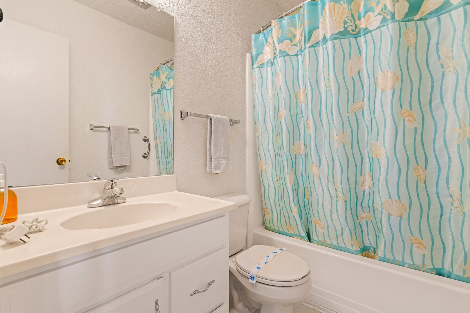 Un bagno con lavandino bianco, specchio e WC. È presente una tenda da doccia a righe blu e bianche.