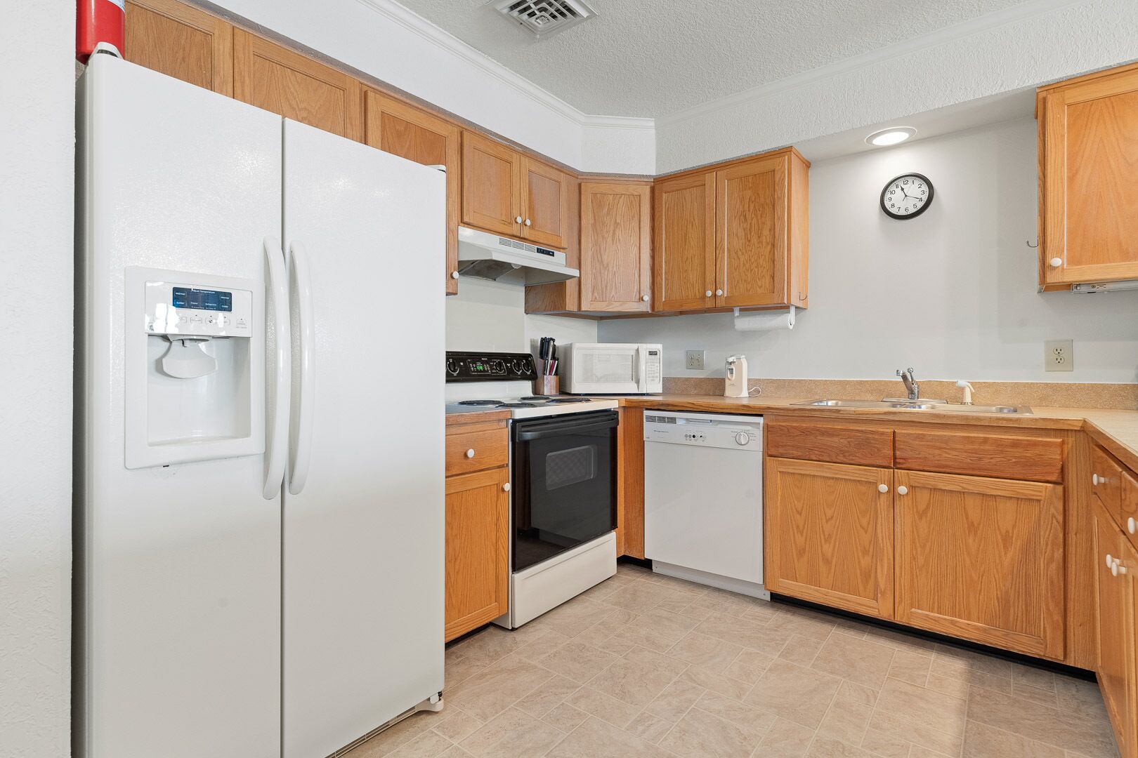 A compact kitchen with wooden cabinets, a white refrigerator, a microwave, an oven, and a dishwasher.