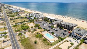 An aerial view of a coastal hotel with a beach view, a parking lot, and a swimming pool. - Oceanfront 3 Bedroom Condo at Golden Strand E3 (Kill Devil Hills)