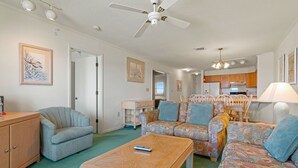 A cozy living room with a sofa set, a wooden coffee table, and a ceiling fan. - Oceanfront 3 Bedroom Condo at Golden Strand E3 (Kill Devil Hills)