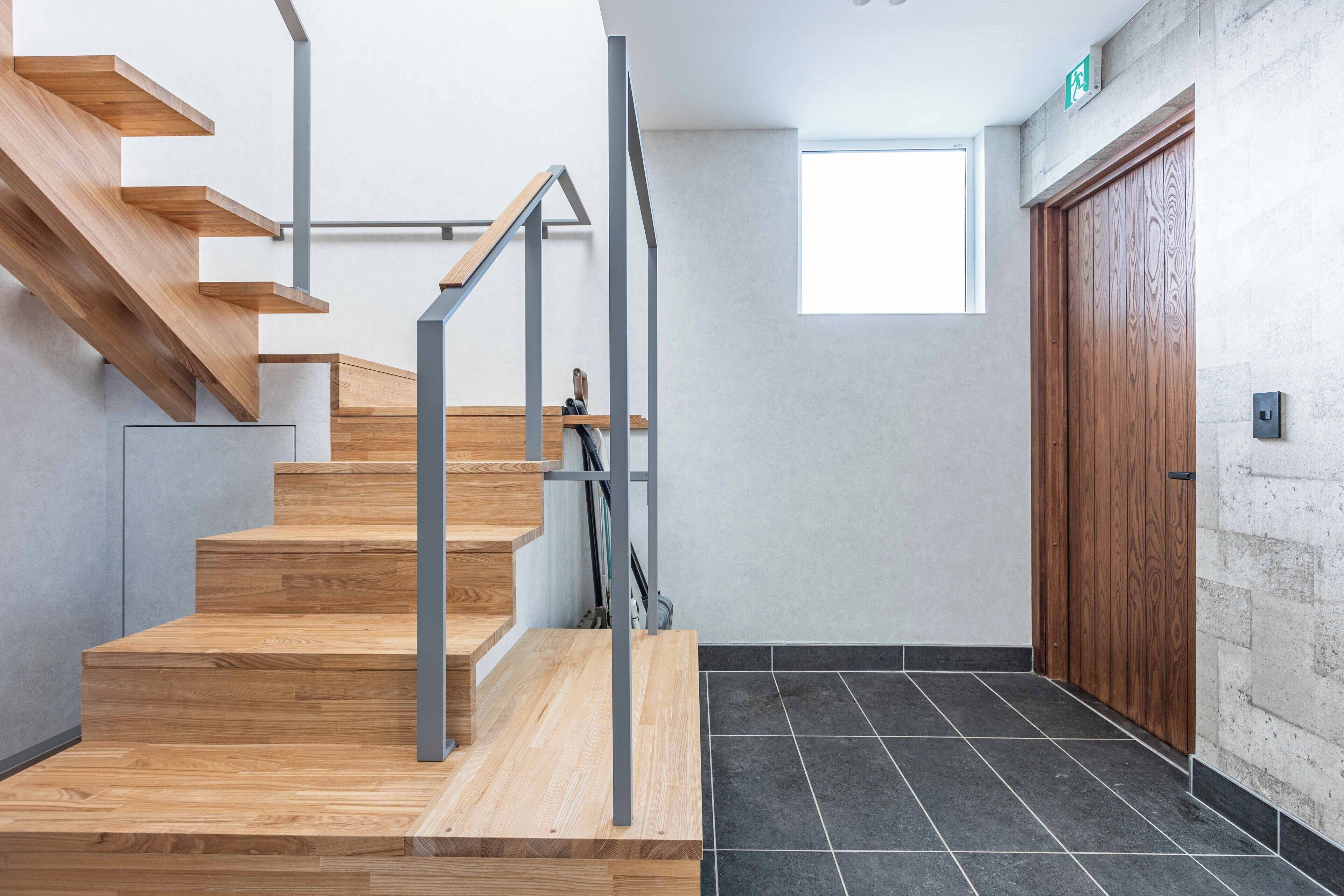 A modern staircase with wooden steps and metal railings, leading to a door with a wooden panel design.