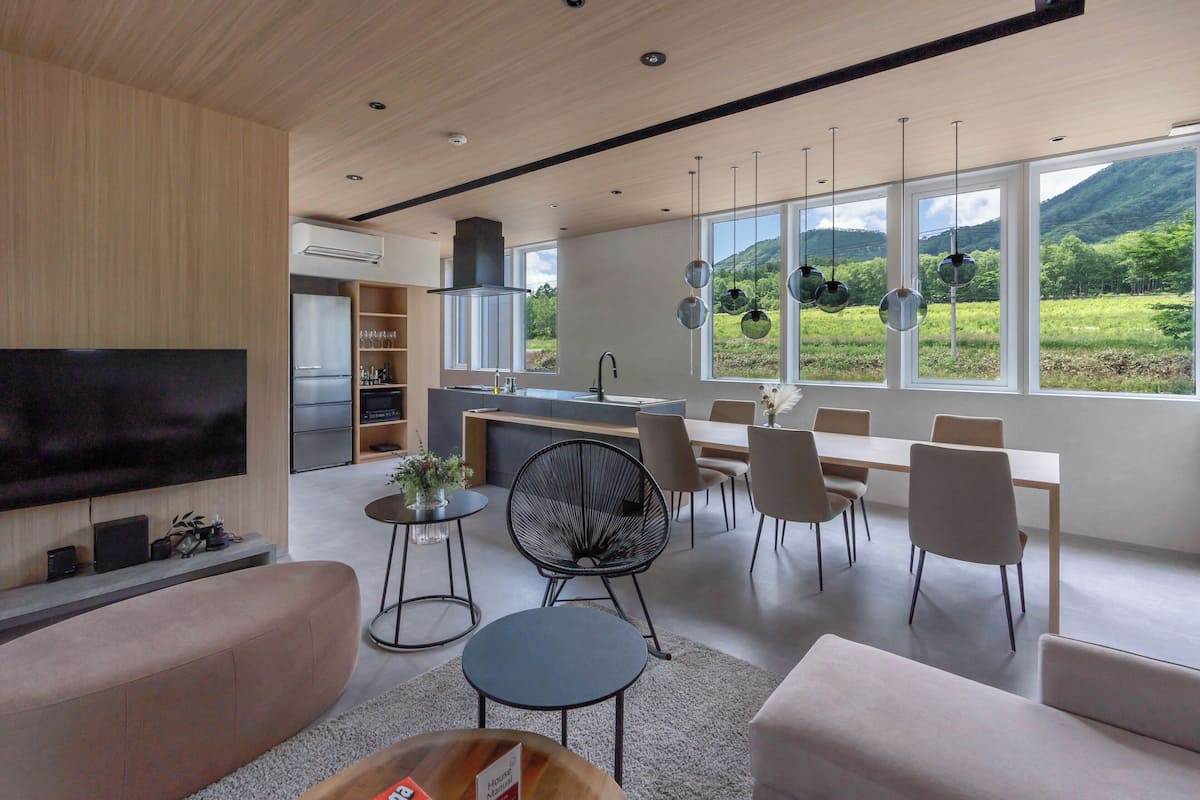 Un salon moderne doté d’un téléviseur à écran plat, de sièges confortables, d’un coin repas avec une grande table et des chaises, et d’une cuisine équipée d’une cuisinière et d’un évier.