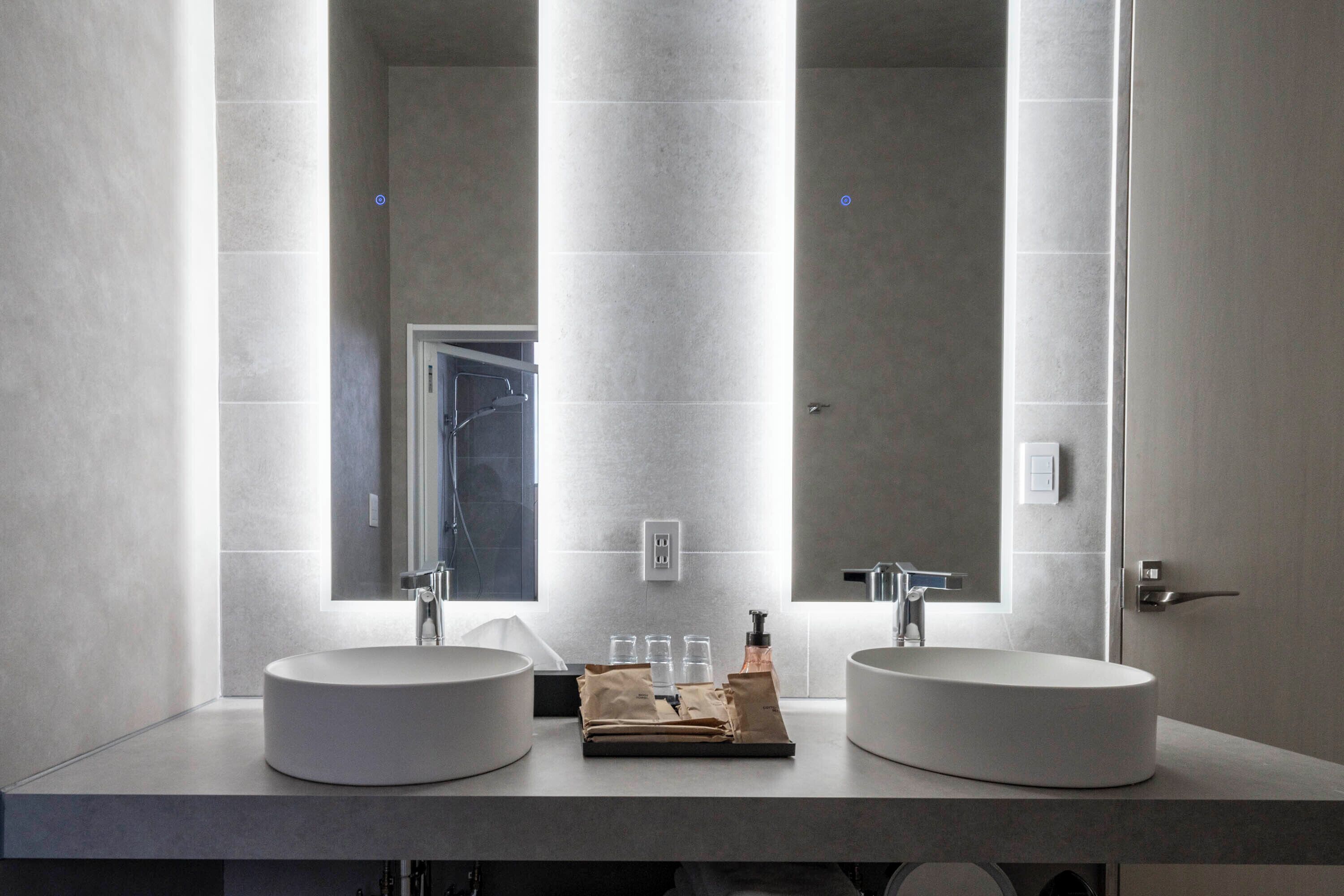 Une salle de bain moderne avec deux vasques rondes, un grand miroir et un porte-serviettes.