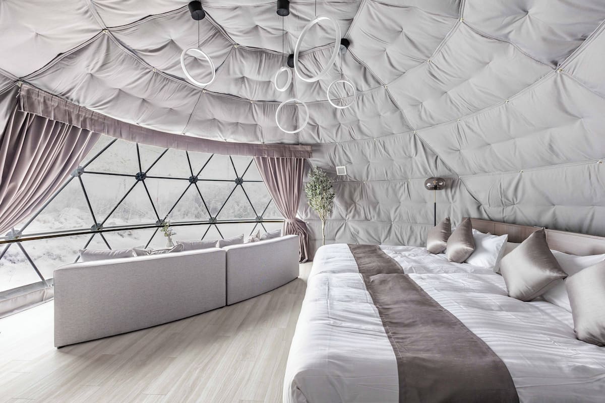 Une chambre moderne dotée d’un grand lit, d’un coin salon et offrant une vue à travers une fenêtre aux motifs géométriques.