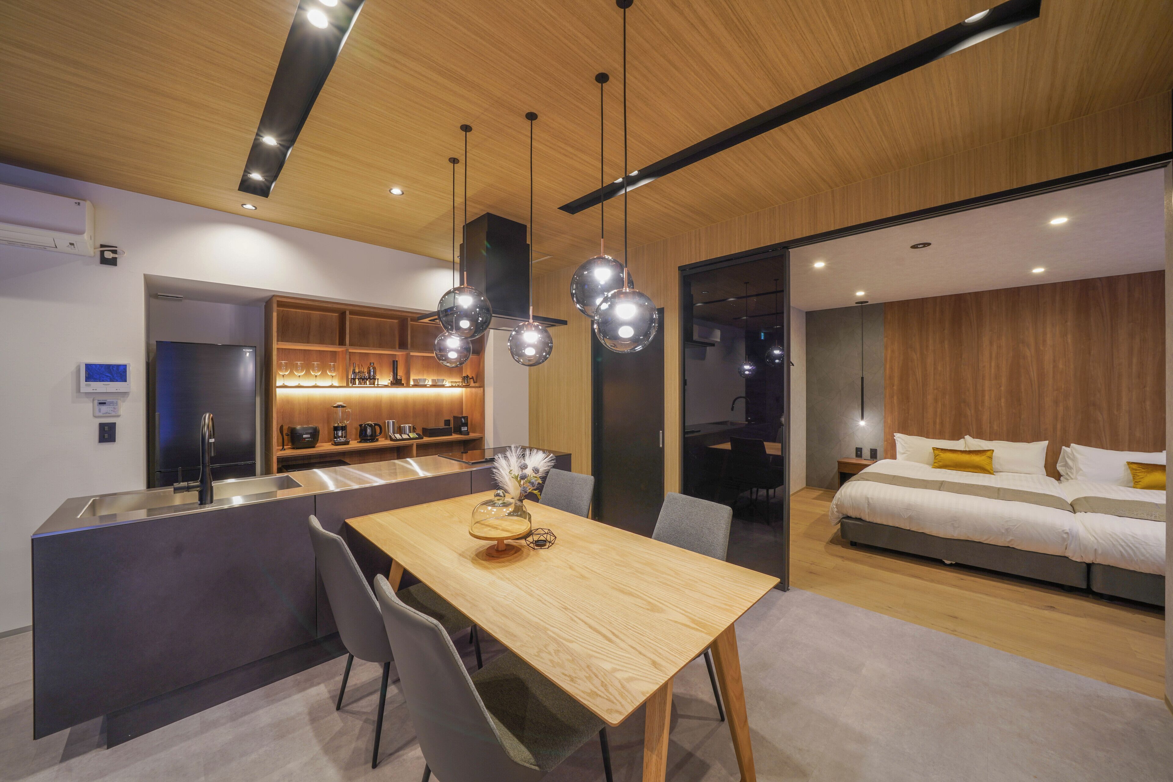 Une cuisine moderne dotée d’un îlot central, un coin repas avec une table en bois et une chambre à coucher avec un lit et des tables de chevet.