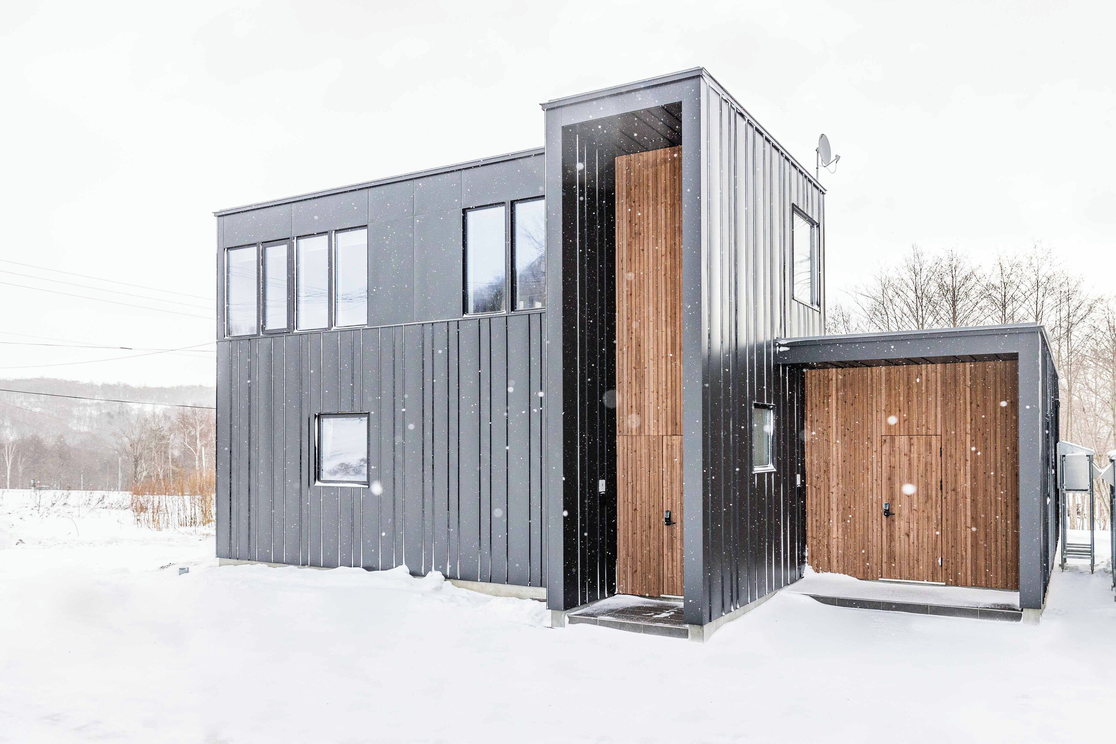 A modern, two-story building with a large wooden door and a smaller door on the side.