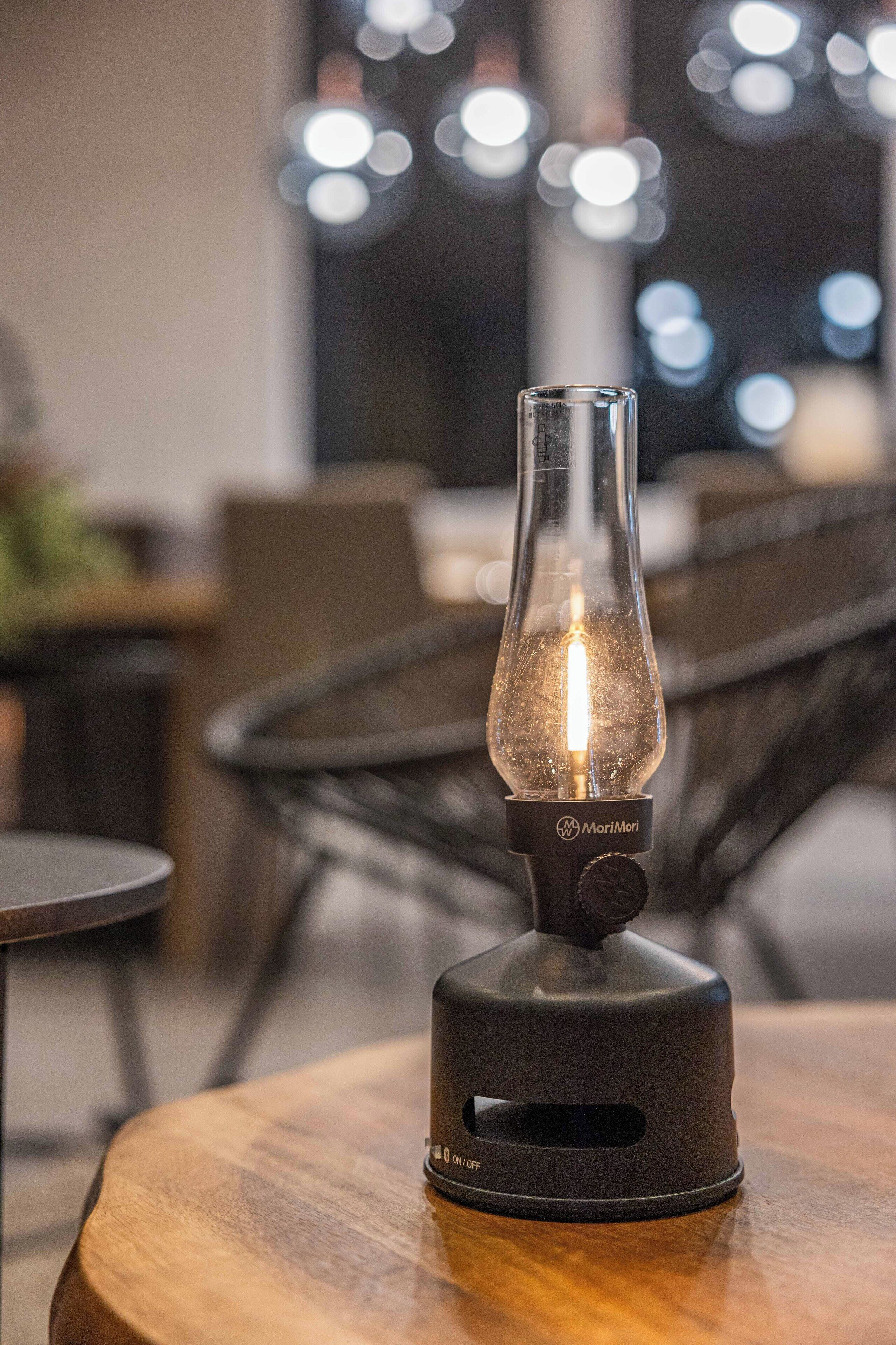 A table lamp with a clear glass shade and a black base, placed on a wooden table in a modern indoor setting.