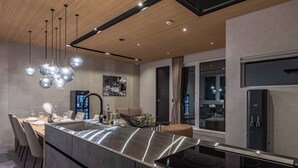 A modern kitchen with a central island, stainless steel appliances, pendant lighting, and a dining area with chairs and a table. - JAPAVISTA RUSUTSU (Rusutsu)