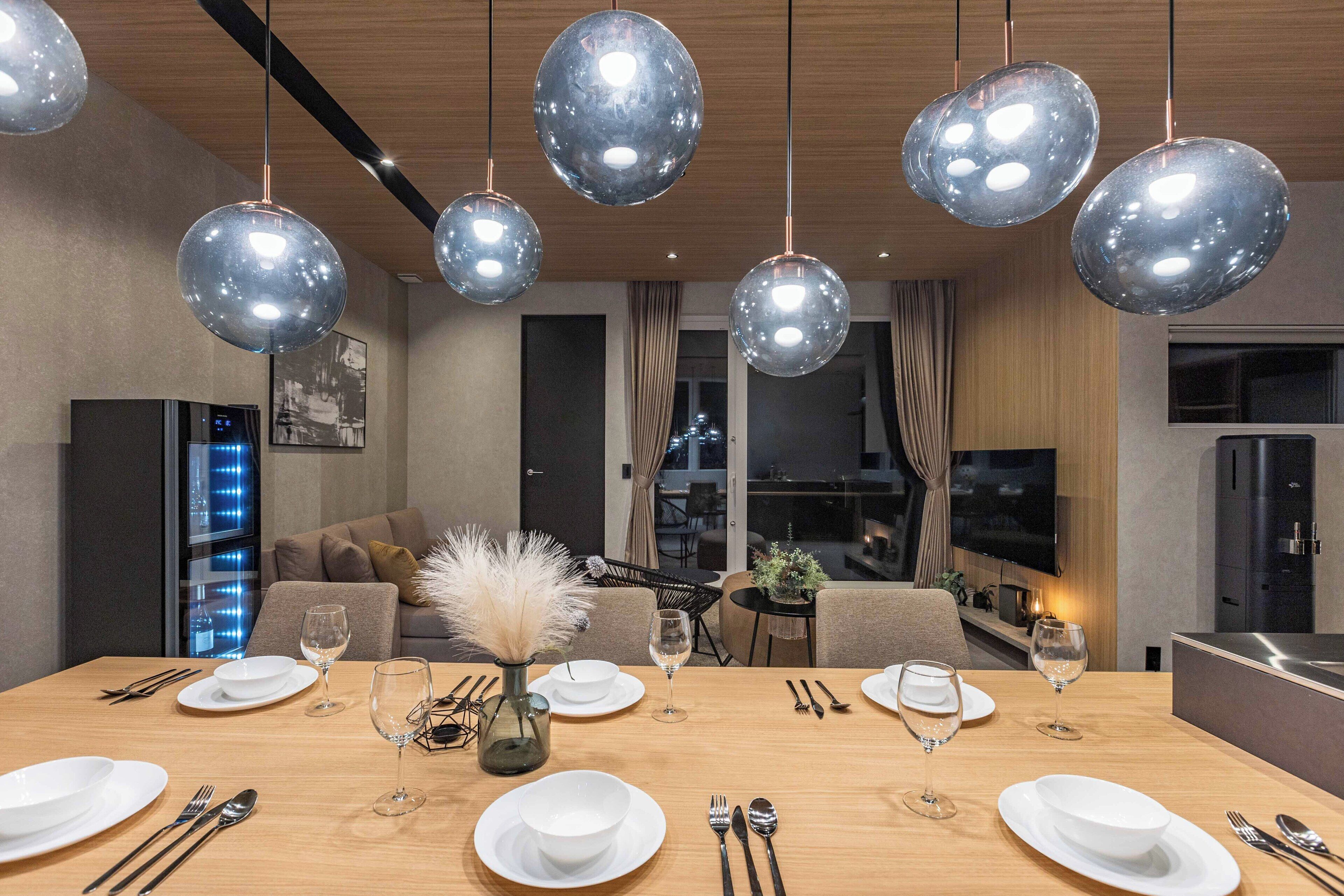 Un espace repas moderne avec une table en bois dressée pour six personnes, entourée de canapés et d’un téléviseur.