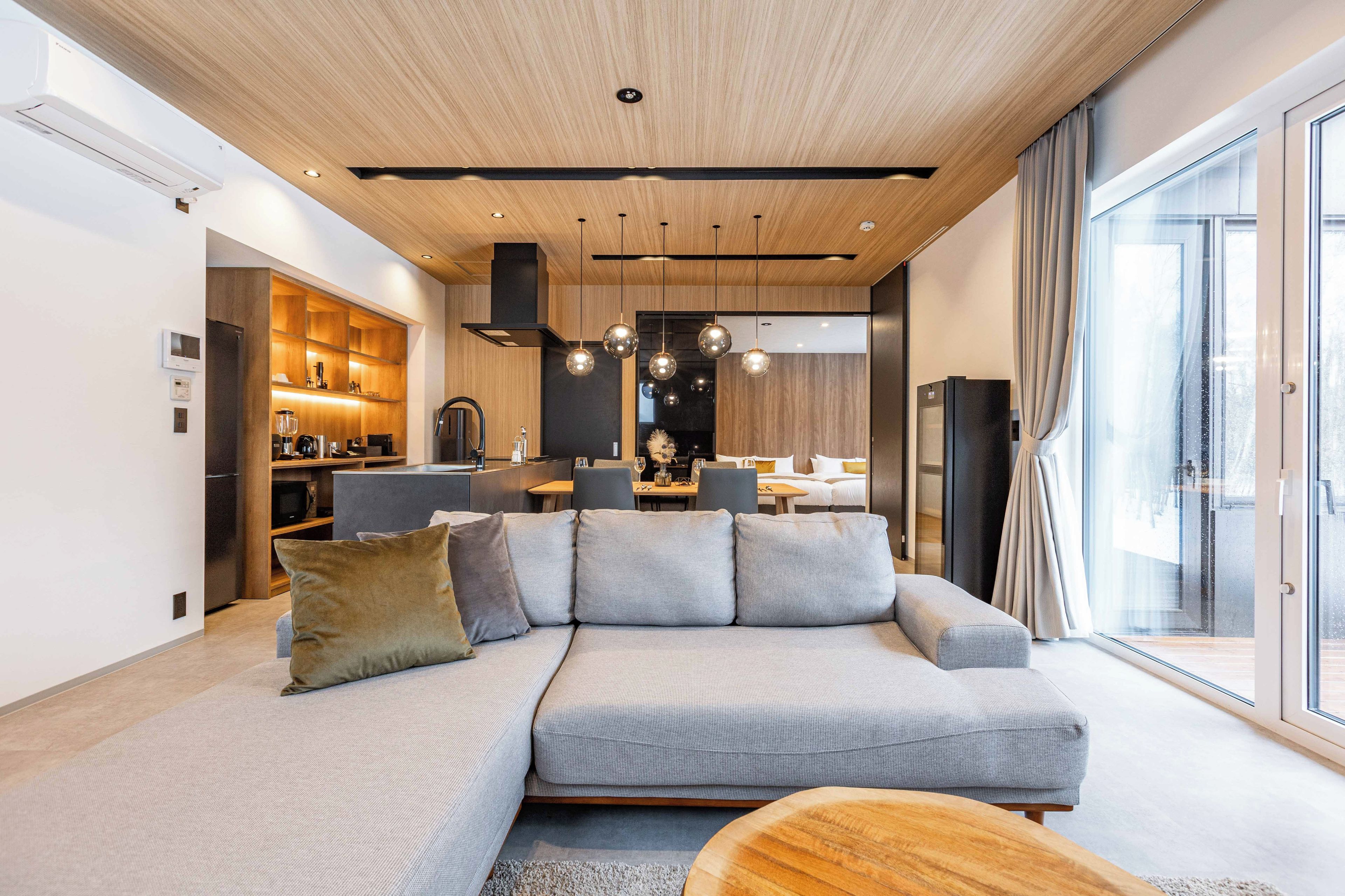 Un salon moderne avec un canapé d’angle, une table basse en bois et une cuisine en arrière-plan.