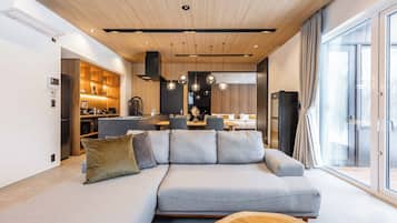 Un salon moderne avec un canapé d’angle, une table basse en bois et une cuisine en arrière-plan.