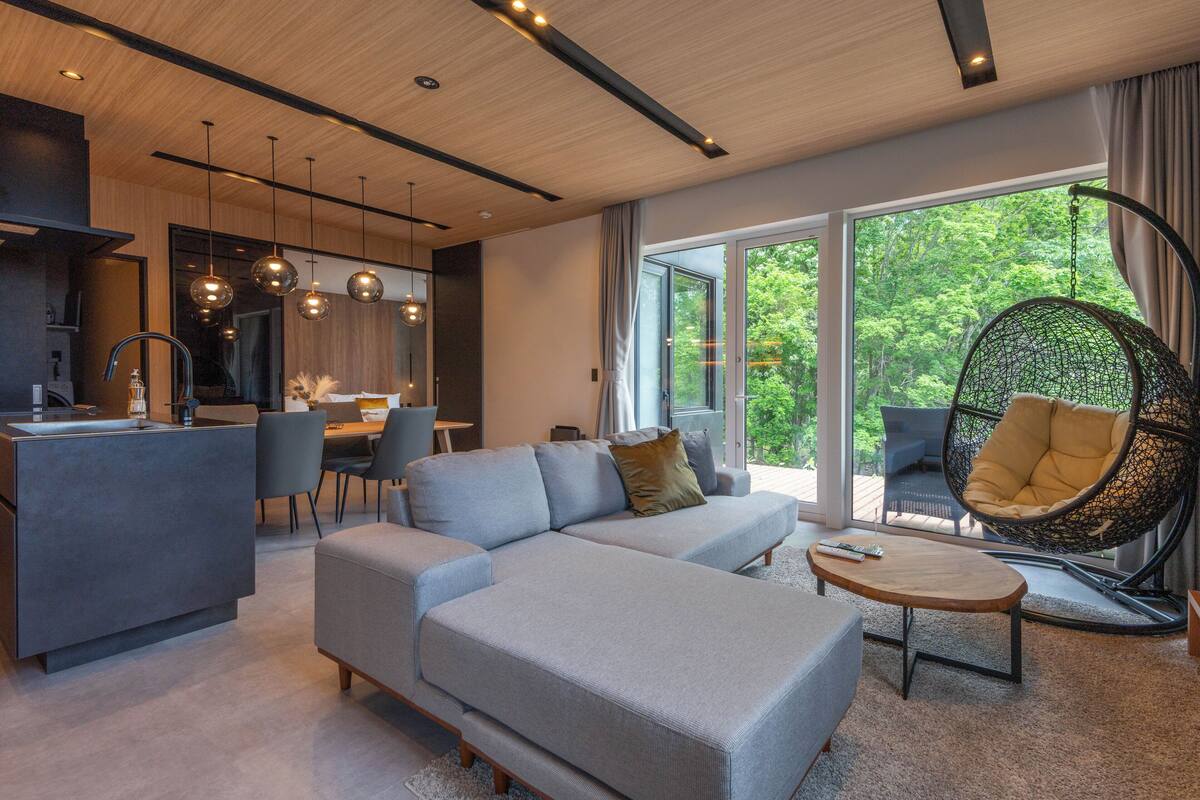 Un salon moderne avec un canapé, une table basse et un fauteuil suspendu. Il y a également un coin cuisine avec une table à manger et des chaises.