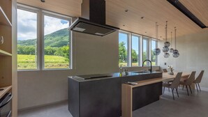 A modern kitchen with a large island, built-in oven, and a view of a green landscape. - JAPAVISTA RUSUTSU (Rusutsu)