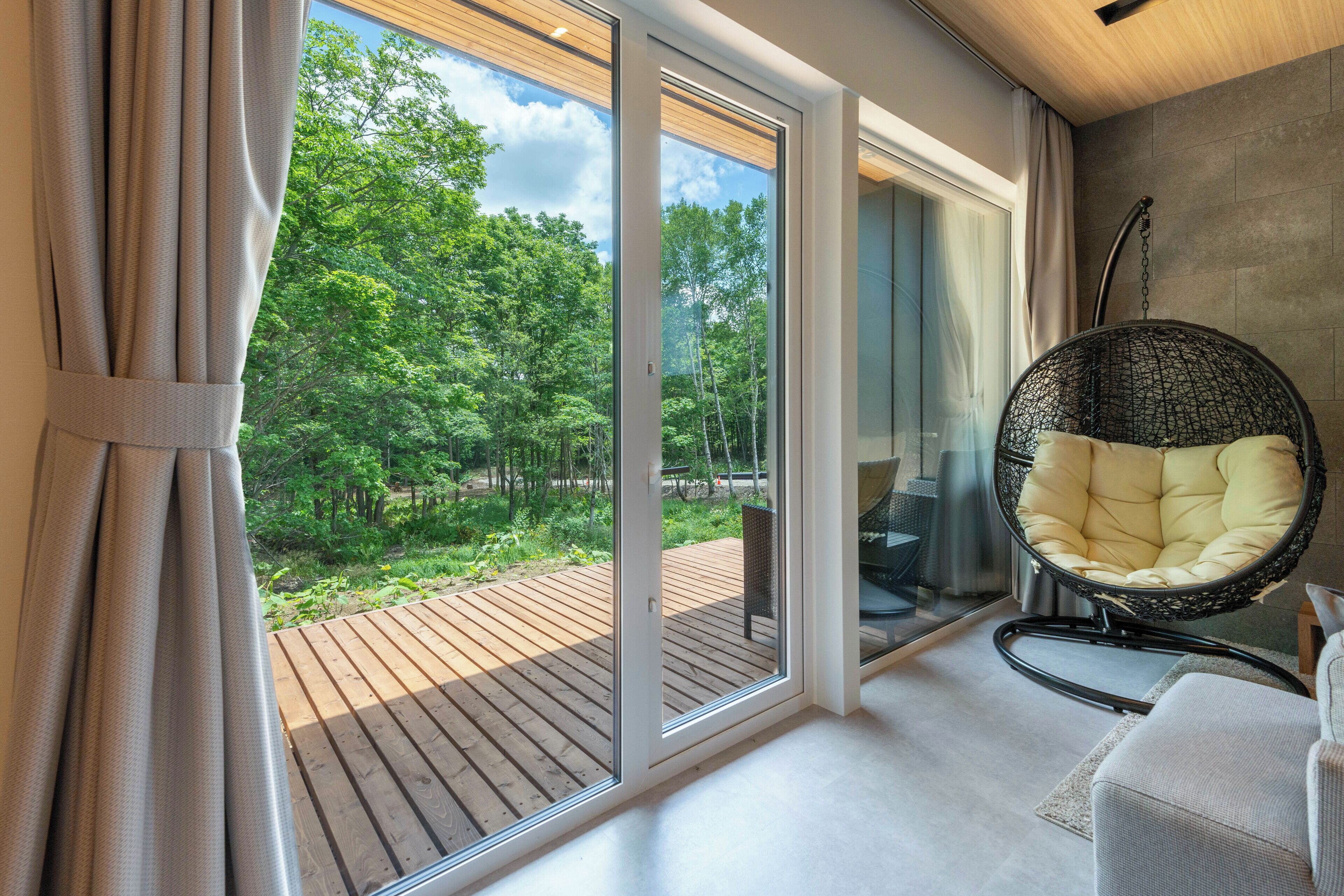 A modern room with a large sliding glass door leading to a wooden deck, a hanging chair, and a sofa.