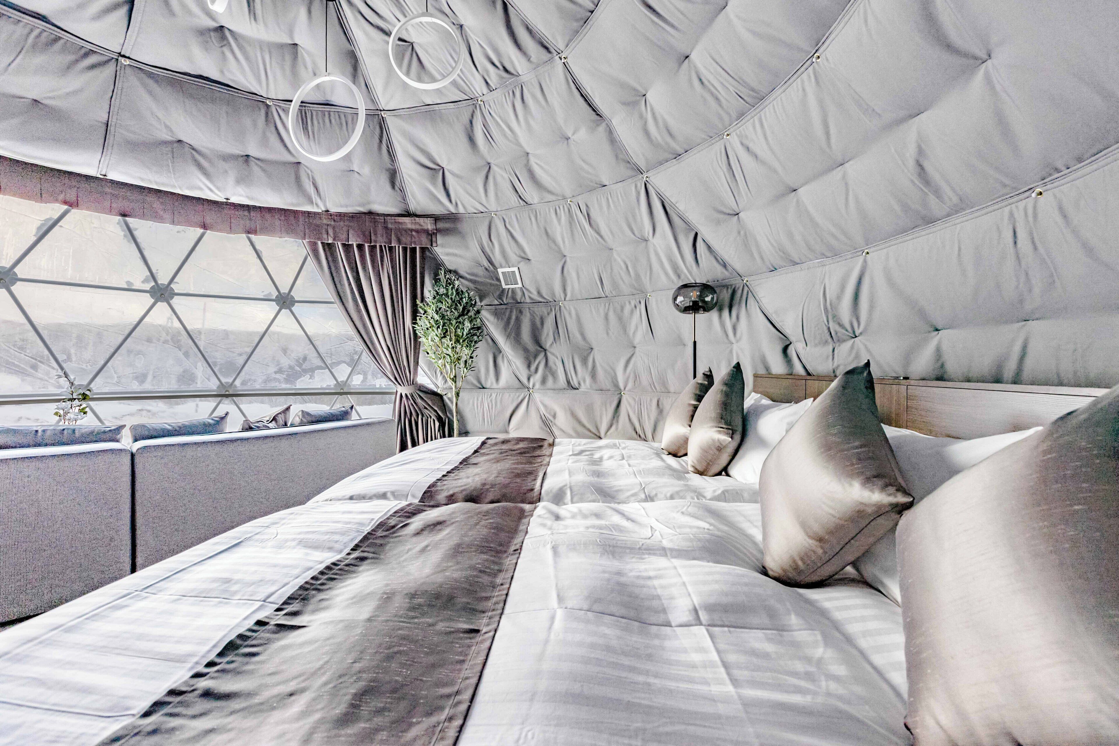 Ein modernes Schlafzimmer mit einem großen Bett, einem Blick durch ein geometrisches Fenster und einem gesteppten Kopfteil.