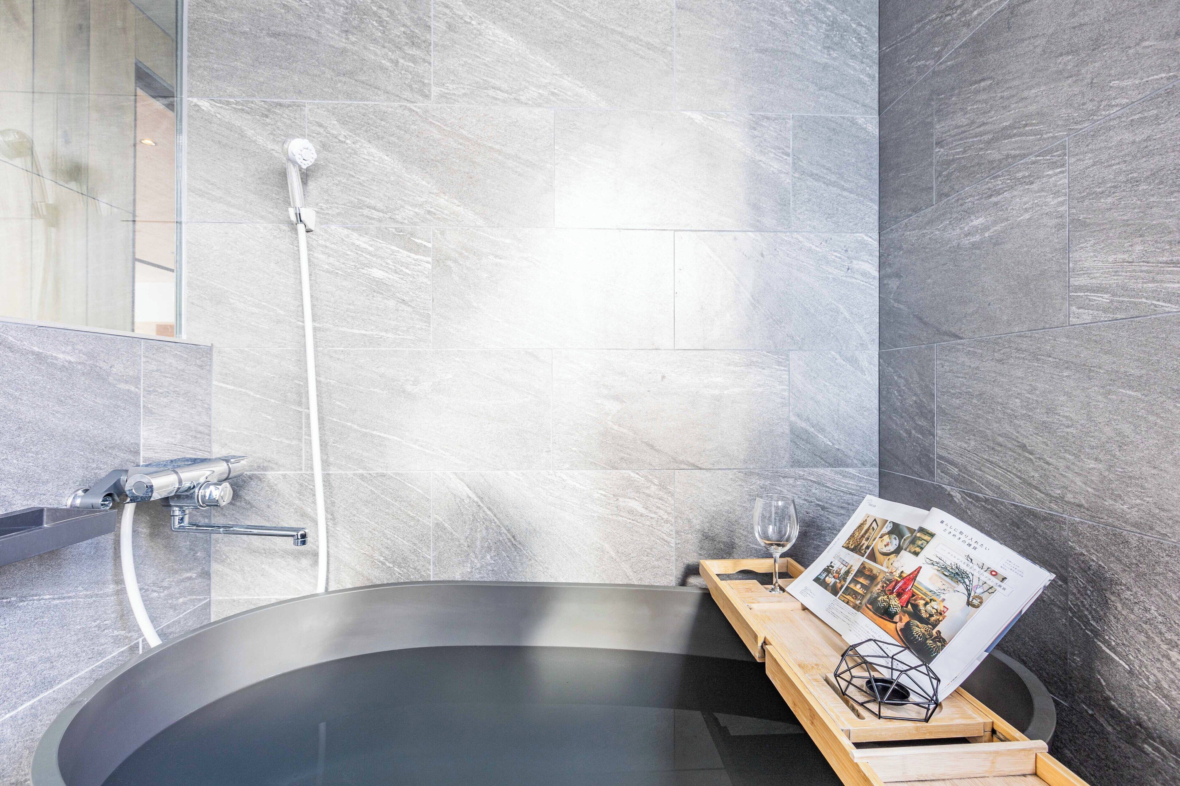 A modern bathroom with a freestanding bathtub, a glass shower enclosure, and a magazine on a wooden tray.